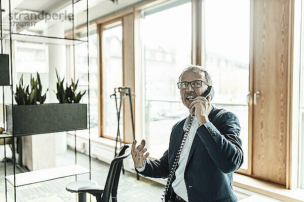 Geschäftsmann gestikuliert beim Telefonieren im Bürokorridor