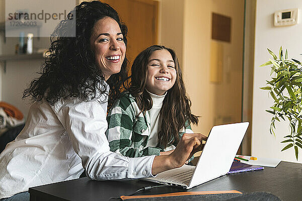 Lächelnde Mutter und Tochter mit Laptop am Wohnzimmertisch sitzend