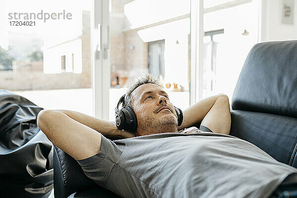 Älterer Mann hört Musik über Kopfhörer  während er auf dem Sofa im Wohnzimmer liegt