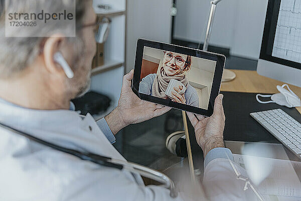 Männlicher Angestellter im Gesundheitswesen im Gespräch mit einem Patienten über ein digitales Tablet  während er in der Arztpraxis sitzt