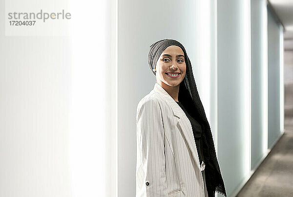 Lächelnde arabische Frau  die wegschaut  während sie in einem Einkaufszentrum an der Wand steht