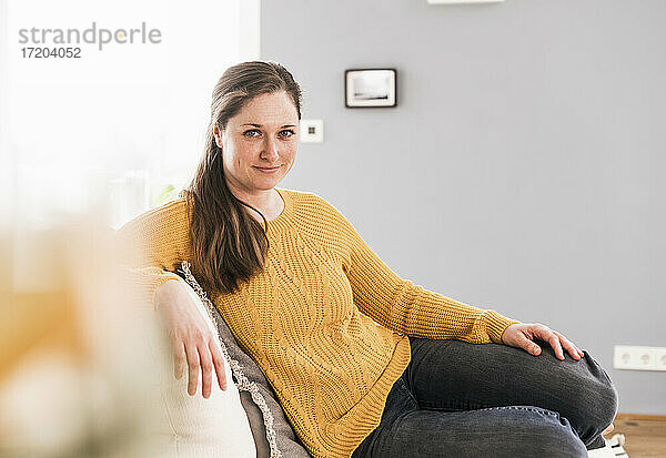 Frau in gelbem Pullover sitzt zu Hause auf dem Sofa