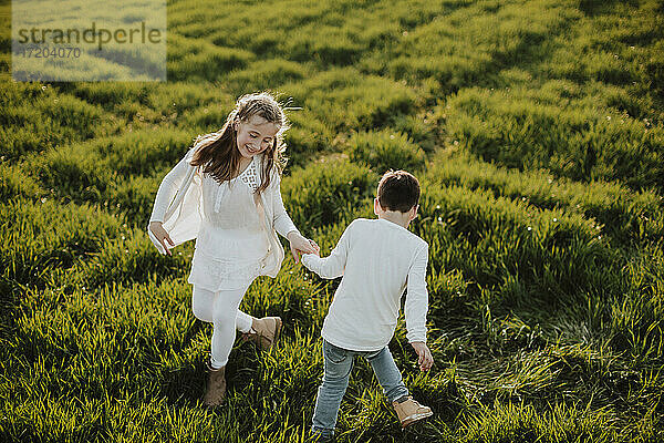 Lächelnd Bruder und Schwester spielen auf Gras während sonnigen Tag