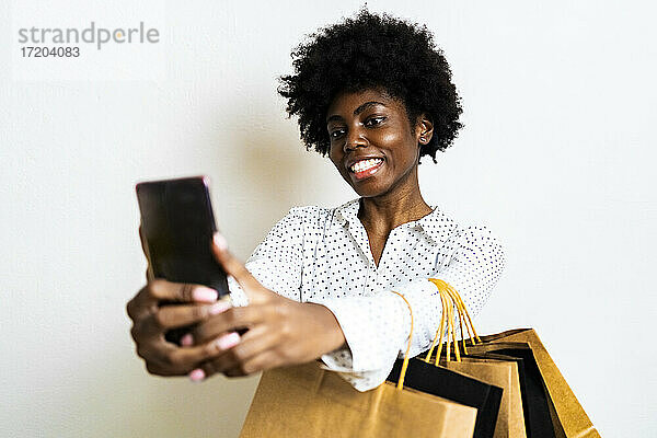 Lächelnde Frau  die ein Selfie mit ihrem Mobiltelefon macht  während sie vor einem weißen Hintergrund steht