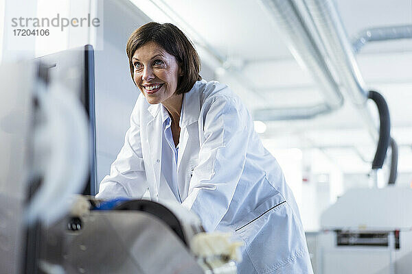 Lächelnde Wissenschaftlerin  die Maschinen im Labor untersucht