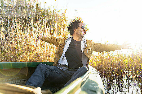 Unbekümmerter Mann mit ausgestreckten Armen  der lächelnd in einem Kanu auf einem Fluss sitzt