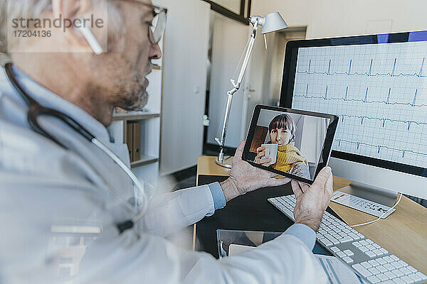 Allgemeinmediziner im Gespräch mit einem Patienten per Videoanruf über ein digitales Tablet in der Arztpraxis