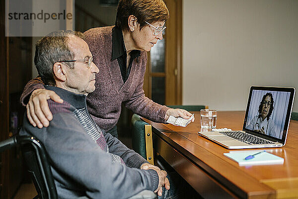 Behinderter älterer Mann und Sozialarbeiter bei einem Videogespräch mit einer Ärztin zu Hause