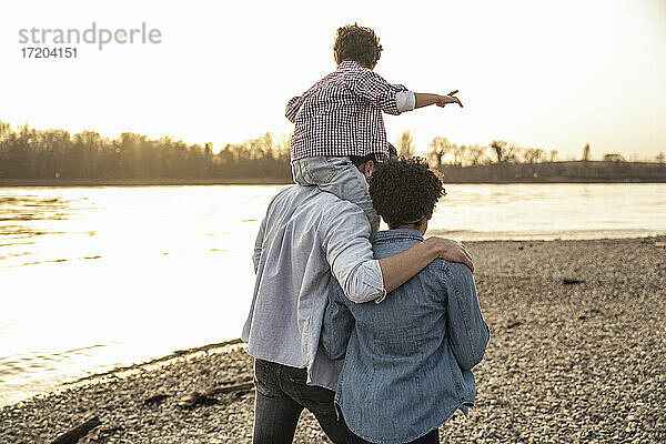 Vater trägt seinen Sohn auf der Schulter  während er mit seiner Mutter am Seeufer spazieren geht
