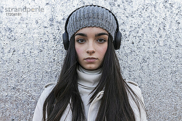 Schönes Teenager-Mädchen mit langen Haaren hört Musik über Kopfhörer gegen silberne Wand