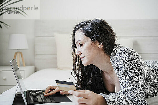 Frau mit Kreditkarte beim Online-Shopping mit Laptop auf dem Bett