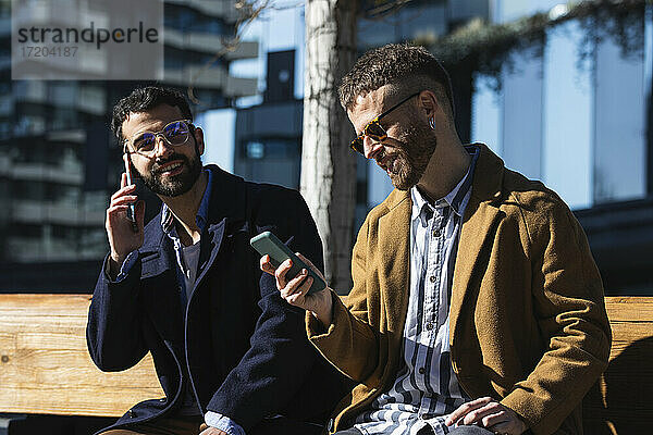 Geschäftsleute benutzen Mobiltelefone  während sie auf einer Bank sitzen