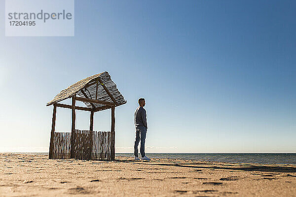 Mann schaut auf das Meer  während er an einem sonnigen Tag am Strand steht
