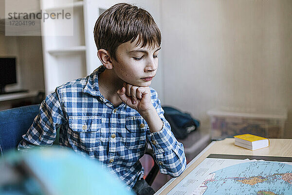 Junge mit Hand am Kinn studiert Karte am Tisch
