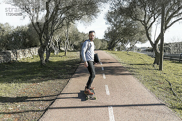 Älterer männlicher Pendler  der an einem sonnigen Tag im Park Skateboard fährt