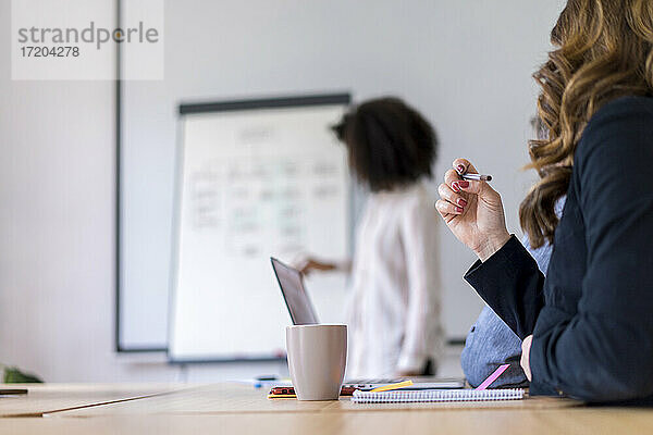 Unternehmerin mit Kaffeetasse am Tisch während einer Sitzung im Sitzungssaal im Büro