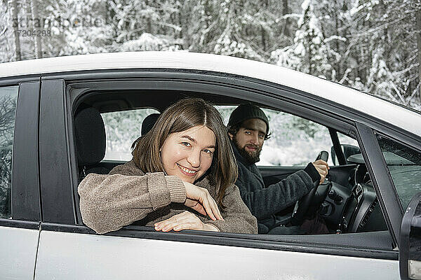 Lächelnde Frau schaut aus dem Fenster  während sie mit einem Mann im Auto sitzt