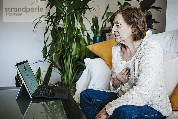 Frau im Gespräch mit Arzt über Videoanruf auf Laptop  während sie zu Hause am Tisch sitzt