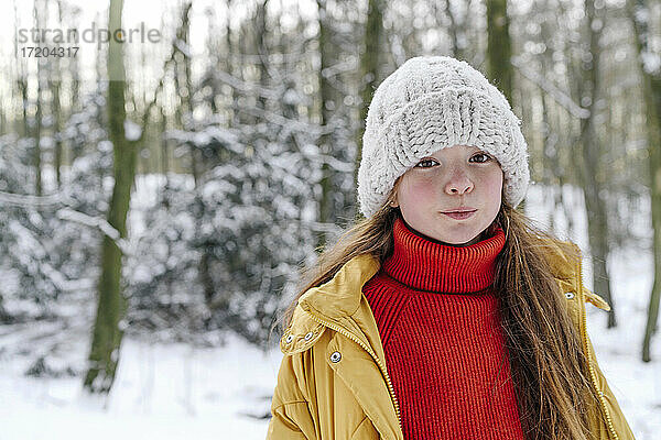 Mädchen mit Strickmütze  das bei Schnee gegen Bäume steht