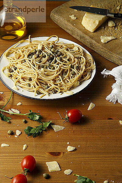 Teller mit frischen Spaghetti mit Kapern inmitten von Koriander und Kirschtomaten auf dem Tisch