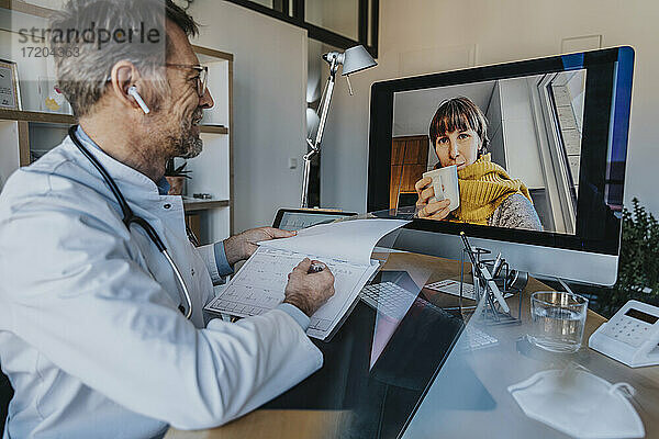 Männlicher Arzt bespricht das Ergebnis der Pulskontrolle mit einem Patienten per Videoanruf über den Computer im Büro