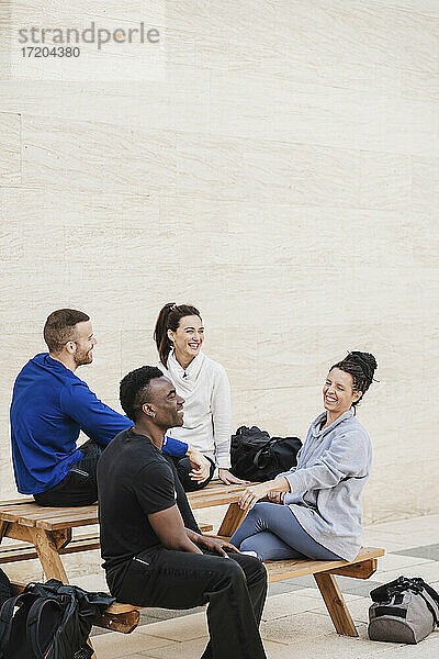 Multiethnische Gruppe von Sportlern  die auf einer Bank sitzen und lachen