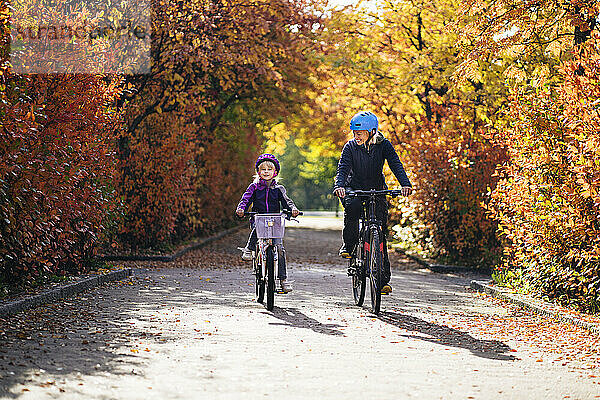 Fröhliche Mutter und Tochter beim Radfahren im Herbst im Park