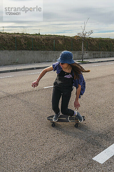 Junge Frau mit Hut fährt mit Skateboard auf der Straße