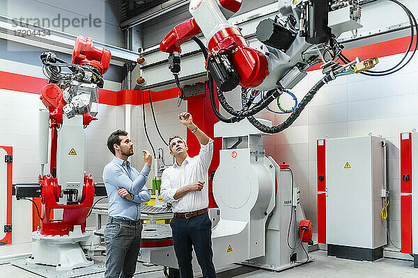 Älterer Unternehmer diskutiert mit einem Kollegen in einer Fabrik über einen Roboterschweißbrenner