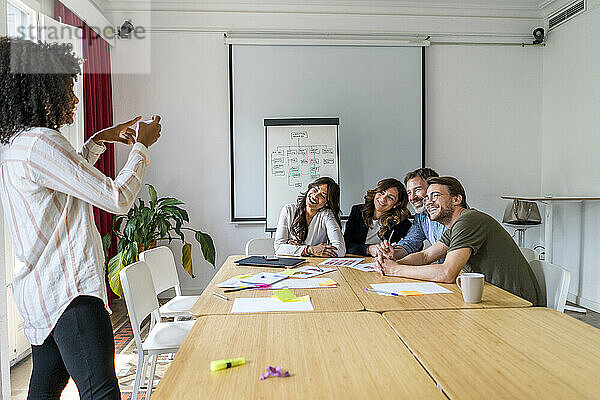Junge afroamerikanische Unternehmerin  die während einer Besprechung im Büro ein Foto von Kollegen macht