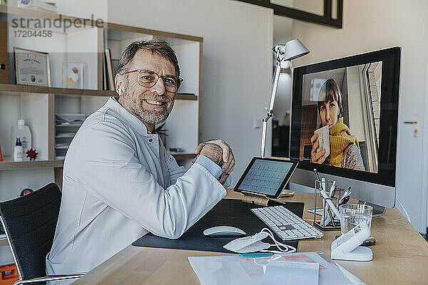 Lächelnder Arzt mit Patientin über Videoanruf am Computer in der Arztpraxis