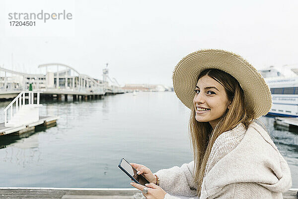 Lächelnde Frau mit Mobiltelefon am Wasser