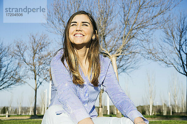Glückliche Frau lächelt  während sie an einem sonnigen Tag im Park sitzt