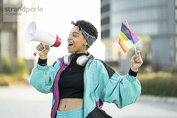 Weibliche LGBTQIA-Demonstrantin hält Regenbogenfahne  während sie durch Megaphon verkündet