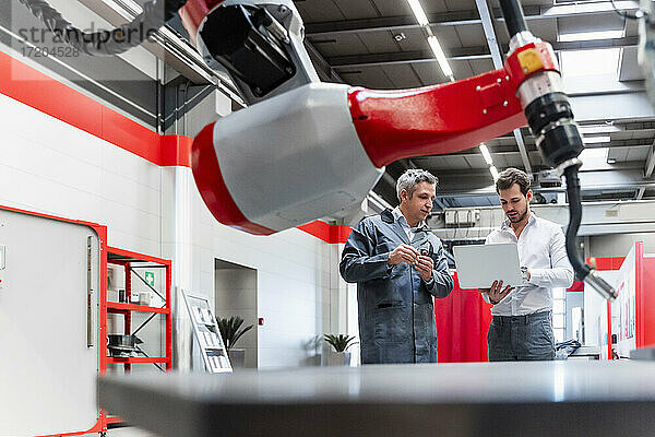 Männliche Unternehmer mit Laptop durch die Robotik in der Fabrik gesehen