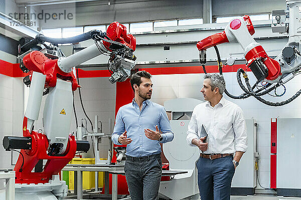 Junger männlicher Automatisierungsingenieur diskutiert mit einem Kollegen über Maschinen in einer Fabrik