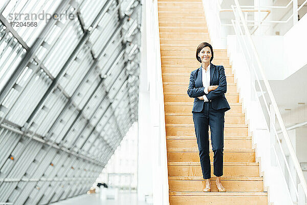 Selbstbewusste Geschäftsfrau mit verschränkten Armen auf einer Treppe im Korridor stehend