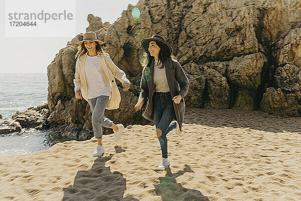 Lächelnde Schwestern laufen auf Sand am Strand