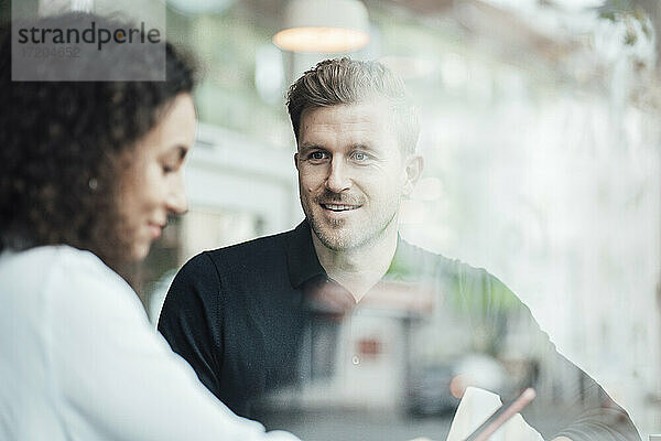 Geschäftsmann sieht einen Kollegen an  der ein Mobiltelefon benutzt  während er in einem Café sitzt