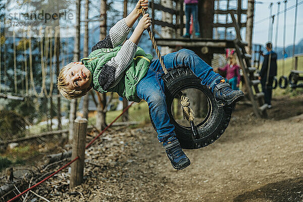 Verspielter Junge schwingt auf einer Reifenschaukel im Hochseilgarten im Wald