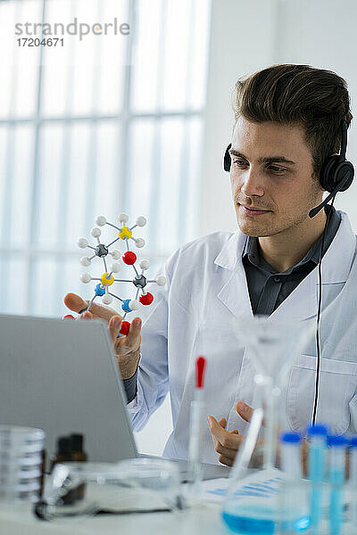 Männlicher Wissenschaftler  der während eines Videogesprächs im Labor eine Molekularstruktur auf einem Laptop zeigt