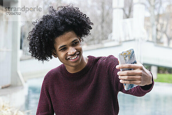 Lächelnder Junge  der ein Selfie mit seinem Handy macht  während er im Freien sitzt