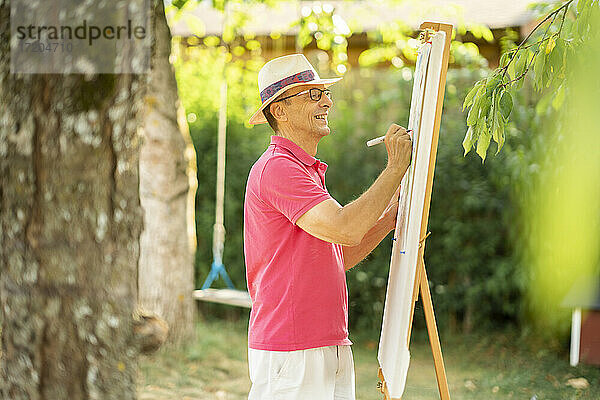 Glücklicher älterer Mann  der im Garten auf einer Leinwand zeichnet