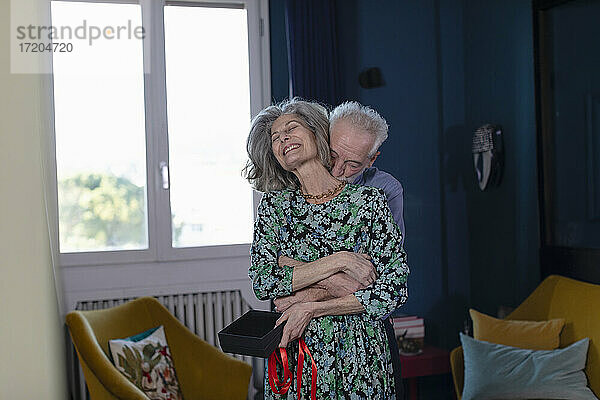 Älterer Mann umarmt lächelnde Frau  während er zu Hause steht