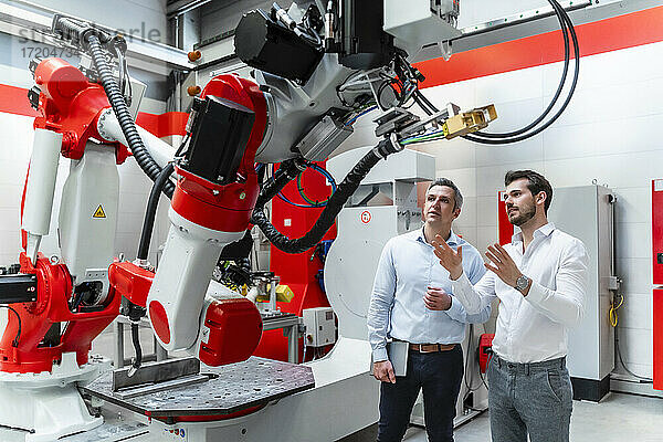 Männliche Ingenieure diskutieren über Robotermaschinen in einer Fabrik