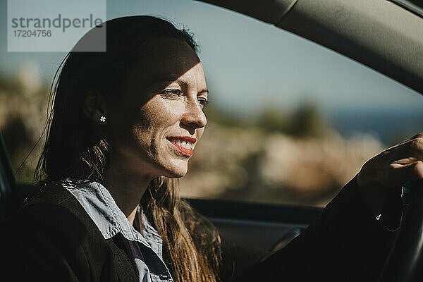 Geschäftsfrau lächelnd beim Autofahren an einem sonnigen Tag