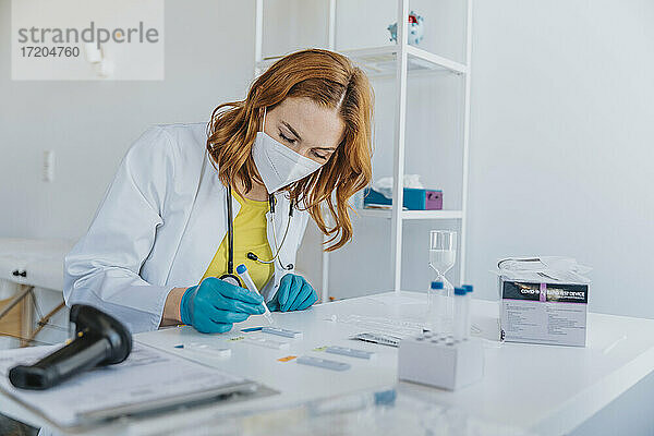 Allgemeinmediziner  der im Untersuchungsraum sitzend Proben auf Testkassetten prüft