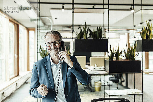 Lächelnder Geschäftsmann mit Brille  der in einem Büro steht und telefoniert