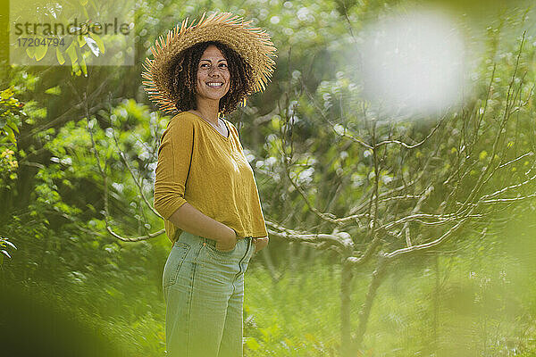 Lächelnde Frau mit Strohhut  die im Garten steht und wegschaut