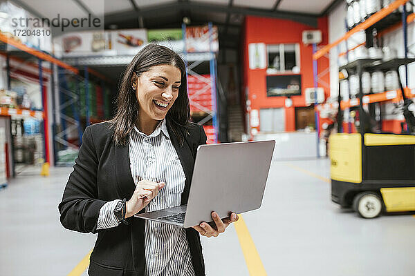 Lächelnde Managerin mit Laptop in einem beleuchteten Vertriebslager